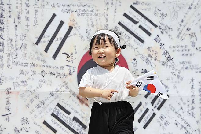 광복군이 서명한 태극기 앞에서 - 태극기를 든 아이가 15일 서울 종로구 인사동에 설치된 ‘한국광복군 서명문 태극기’ 전시물 앞에서 웃고 있다. 이 태극기는 광복군 제3지대에서 활동하던 문웅명 지사가 간직한 것으로, 광복군들의 서명과 조국 독립을 위한 결의를 다지는 글귀가 적혀 있다. 이날 제78주년 광복절을 맞아 보신각 타종 등 전국 곳곳에서 각종 행사가 열렸다. /연합뉴스