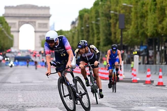 8월 19일 파리에서 열린 2023 세계 장애인 트라이애슬론 올림픽 테스트 이벤트에서 한국의 김황태(가운데)가 프랑스 선수 쥘 리브스타인(왼쪽)과 개선문을 배경으로 사이클을 타고 있다. 두 팔이 없는 김황태는 의수를 착용하고 사이클을 탄다. /AFP 연합뉴스