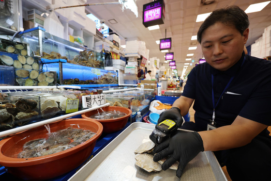 An official from Noryangjin Fisheries Wholesale Market's market monitoring unit conducts a radioactivity check on clams at the fisheries market in Dongjak District, southern Seoul, on Wednesday, a day before Japan's release of Fukushima wastewater. [YONHAP]