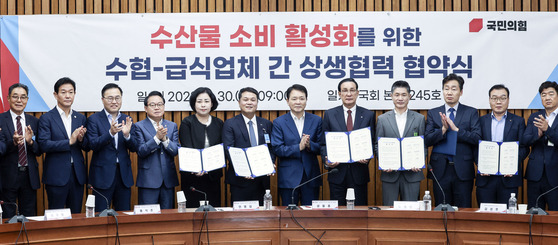 Rep. Sung Il-jong of the People Power Party (PPP) along with the representatives from the National Federation of Fisheries Cooperatives and catering companies take a photo after a agreement ceremony for boosting seafood consumption at the National Assembly on Wednesday. [KIM SEONG-RYONG]