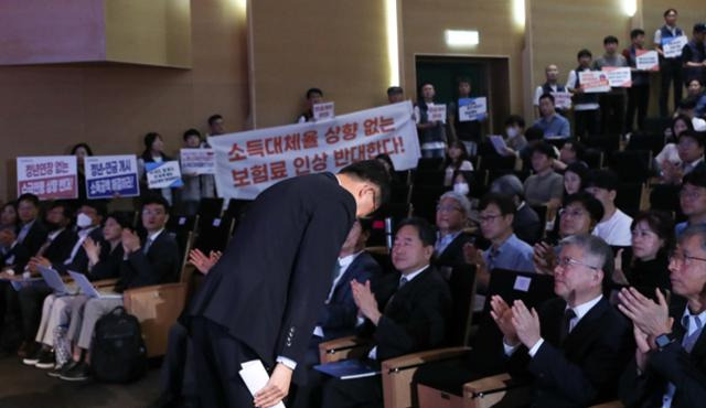 1일 서울 강남구 코엑스에서 열린 5차 국민연금 재정계산 공청회에서 고개 숙여 인사하는 이기일 보건복지부 1차관 뒤로 양대노총 조합원들이 보험료 인상을 규탄하는 플래카드와 손피켓을 펼치고 있다. 뉴시스