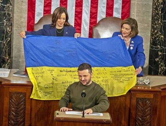 21일(현지시간) 카멀라 해리스 미 부통령(왼쪽)과 낸시 펠로시 미 하원의장(오른쪽)이 미국 워싱턴DC 하원 본회의장에서 볼로디미르 젤렌스키 우크라이나 대통령이 선물한 도네츠크주 바흐무트 최전방 부대 병사들의 자필 서명이 적힌 우크라이나 국기를 펼쳐보이고 있다. 전쟁 300일 만에 처음으로 외국행을 강행한 젤렌스키 대통령은 이날 미 의회에서 연설했다. 2022.12.22 UPI 연합뉴스