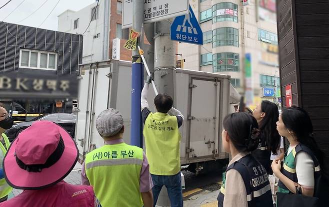 부산 동래구가 개학기를 맞아 지난 13일 안락교차로 부산은행 앞에서 ‘불법 광고물 일제정비 캠페인’을 진행한 가운데 한 참여자가 불법 광고물을 제거하고 있다. 사진제공ㅣ부산 동래구