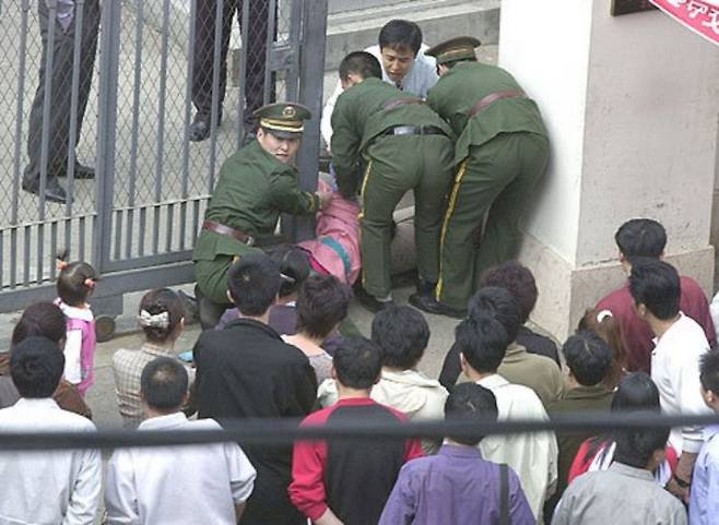 2002년 5월 중국 선양의 일본영사관으로 진입을 시도하던 탈북민이 중국 공안에 의해 강제로로 끌려 나오고 있다. 왼쪽에 선 여자아이는 끌려 나오는 탈북여성의 두 살배기 딸이다. [이미지출처=연합뉴스]