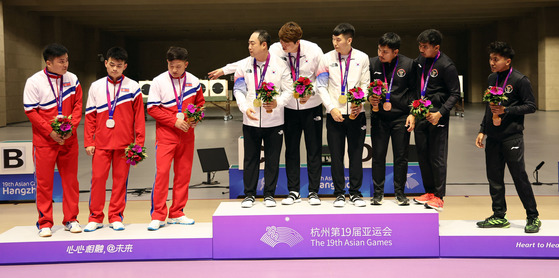 The South Korean men’s team that won the gold medal in the 10-meter target range running event, center, urges the North Korean team that won the silver medal, left, to join a group photo during the medal ceremony at Fuyang Yinhu Sports Center in Hangzhou, China, on Monday. The North Koreans refused the gesture. A similar situation happened in judo the same day when the North Korean judoka Kim Chol-gwang refused to shake the hand of his South Korean opponent, Kang Heon-cheol, in a round of 16 match in the men’s 76-kilogram division. The Asian Games in Hangzhou is the first international multi-sport event that the North Koreans have attended in five years since the Jakarta Palembang 2018 Asian Games [YONHAP]