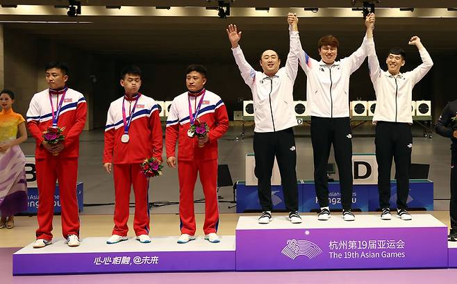 지난 25일 중국 항저우 푸양 인후 스포츠센터에서 열린 항저우 아시안게임 남자 사격 10m 러닝타깃 단체전에서 금메달을 획득한 한국의 하광철(왼쪽 네 번째부터), 정유진, 곽용빈이 시상대에 오르고 있다. 은메달을 획득한 박명원, 유성준, 권광일 등 북한 선수들이 굳은 표정을 짓고 있다. 연합뉴스