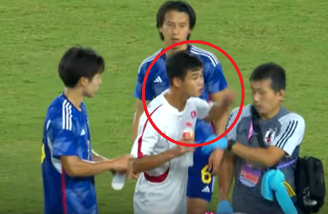 북한의 2003년생 수비수 김유성(빨간 동그라미)이 자국 선수들에게 물을 주려고 아이스박스를 들고 온 일본 스태프에게서 물병을 빼앗고 있다.