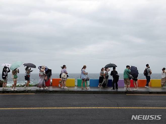 [제주=뉴시스] 오영재 기자 = 제주시 도두동 무지개해안도로에서 우산을 쓴 관광객들이 사진을 찍고 있다. 뉴시스DB. oyj4343@newsis.com