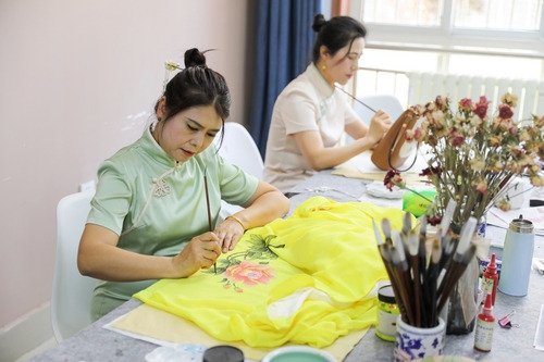 A female painter is painting peony on silk at the workshop.