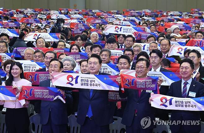 '분단을 넘어 글로벌 중추국가' (고양=연합뉴스) 임헌정 기자 = 윤석열 대통령이 28일 경기 고양시 킨텍스에서 열린 제21기 민주평화통일자문회의 전체회의에서 참석자들과 함께 '분단을 넘어 글로벌 중추국가' 슬로건이 적힌 수건을 들고 기념 촬영을 하고 있다.    2023.11.28  [대통령실통신사진기자단] kane@yna.co.kr