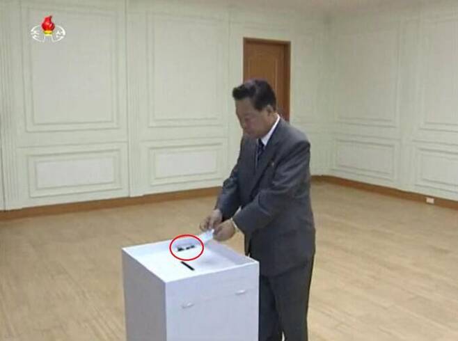 투표실에서 투표하는 투표자. 투표실은 하나의 방이며 투표함 위에 볼펜(빨간 원)이 놓여 있다. (조선중앙TV, 2015년 7월)