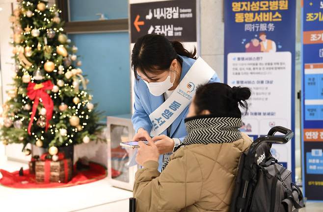 명지성모병원이 동행서비스를 시행하고 있는 가운데, 한 안내 직원이 동행서비스 도움을 위해 환자와 이야기를 나누고 있다.