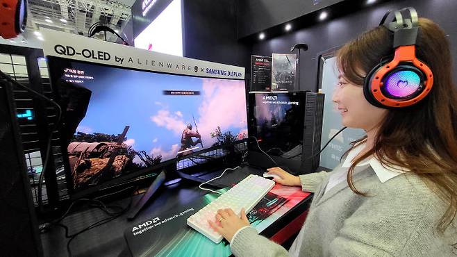 삼성디스플레이 모델이 지스타 2023 AMD 부스에 전시된 ‘에일리언웨어 34 커브드 QD-OLED 게이밍 모니터’로 대규모 이용자 간 대전 ‘워헤이븐’을 체험하고 있다. (사진=삼성디스플레이)