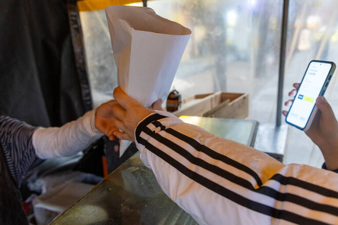 2023년 12월6일 서울 마포구의 한 포장마차에서 손님이 카카오페이로 송금한 화면을 보여주고 봉지를 받아들고 있다. 박승화 기자