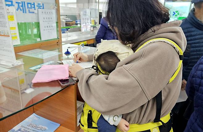 지난 13일 오후 서울 강남구 운전면허시험장에서 한 여성이 아이를 안고 운전면허증 적성검사·갱신 등의 업무를 보기 위해 서류를 작성하고 있다. /남강호 기자
