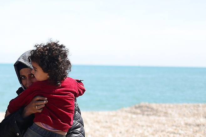 지난 8월16일(현지시간) 영불해협을 건너 영국 남동부 던게네스 해변에 도착한 한 난민 여성이 보트에서 내린 뒤 아이를 품에 안고 있다. AFP연합뉴스