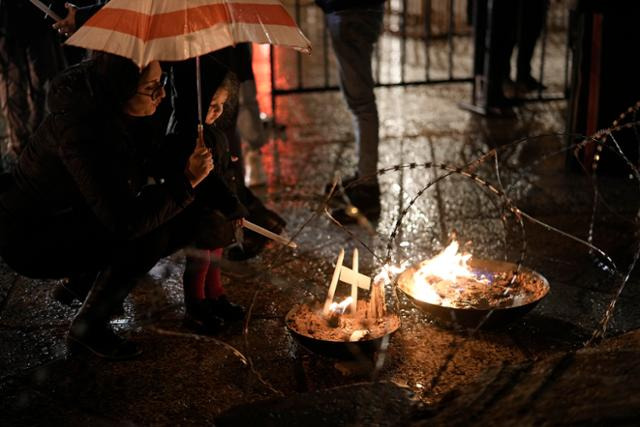 23일 요르단강 서안지구 베들레헴에 있는 예수 탄생 교회 옆 구유 광장에 마련된 성탄 장식 앞에서 한 여성과 아이가 화톳불을 쬐고 있다. 성탄 장식은 이스라엘군의 공격으로 숨진 가자지구 희생자를 추모하고 평화가 오기를 기원하는 바람을 담아 철조망 등으로 장식됐다. 베들레헴=AP 연합뉴스