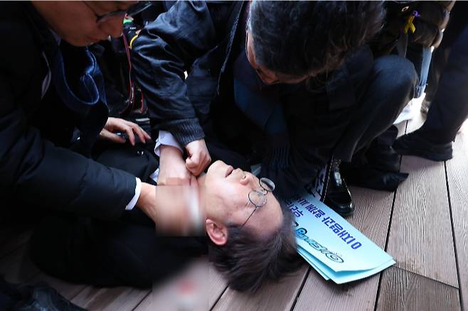 더불어민주당 이재명 대표가 2일 부산 가덕도 신공항 부지를 둘러본 후 기자들과 문답을 진행하던 중 왼쪽 목 부위에 습격을 당해 피를 흘린 채 쓰러져 있다. 연합뉴스