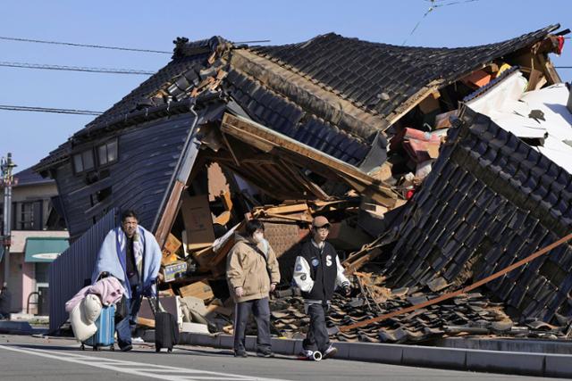 새해 첫날 일본 이시카와현에서 규모 7.6의 강진이 발생하고 하루 뒤인 2일 와지마시에서 한 남성이 이불과 베개, 여행용 가방을 챙겨 지진으로 무너진 집을 지나가고 있다. 와지마=AP·교도 연합뉴스