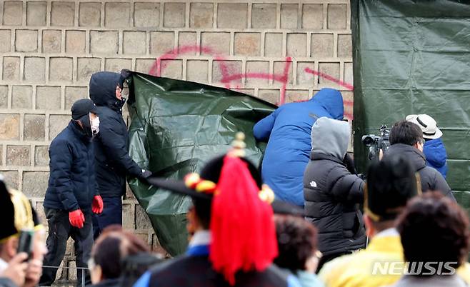 [서울=뉴시스] 김금보 기자 = 문화재청 궁능유적본부 직원들이 16일 오전 서울 종로구 국립고궁박물관 방향 경복궁 서편에서 스프레이 낙서로 훼손된 담벼락을 천으로 덮고 있다. 2023.12.16. kgb@newsis.com