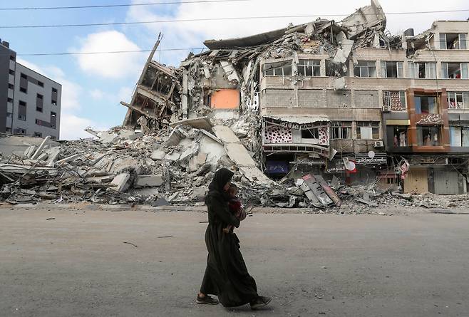 14일(현지 시각) 가자지구 안에서 이스라엘의 폭격으로 무너진 건물 앞을 한 여성이 지나가고 있다./로이터 연합뉴스