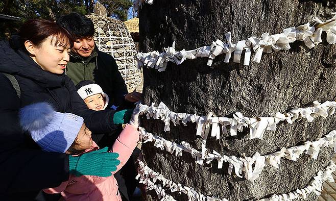설을 앞두고 경기 용인시 한국민속촌을 찾은 한 가족이 새해 소망을 적은 소원지를 달고 있다.