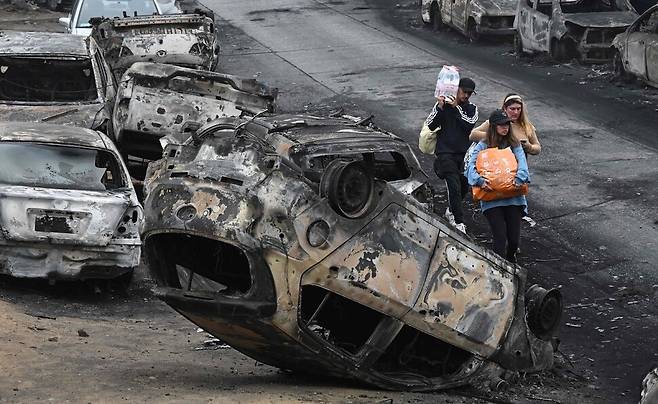 이재민들이 식수와 비상용품을 들고 불에 탄 자동차 사이를 빠져나가고 있다. AFP 연합뉴스