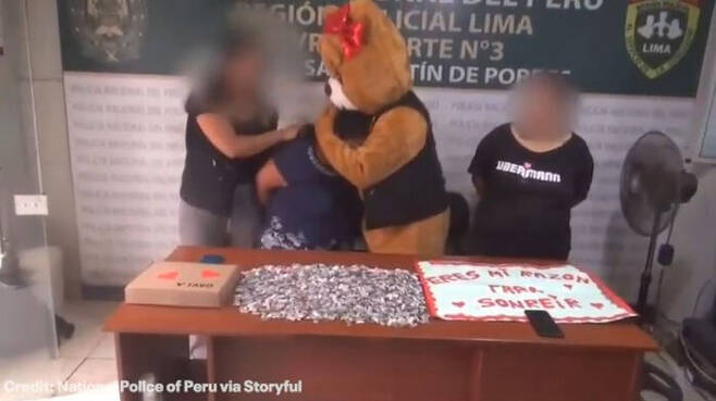 곰인형 탈을 쓴 경찰관이 체포한 용의자들과 함께 작전에 사용했던 초콜릿 상자 앞에서 사진 찍은 모습. (사진= 페루국립경찰(Policia Nacional del Peru, PNP)제공, Storyful)