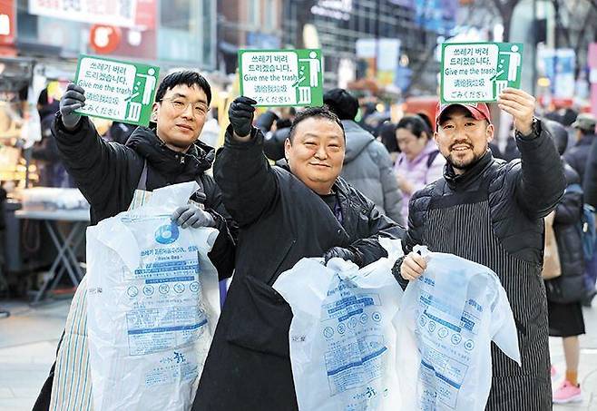 지난 25일 서울 중구 명동 거리에서 노점 상인들이 4개 국어로 ‘쓰레기 버려드리겠습니다’라고 적힌 초록색 안내 팻말과 종량제 쓰레기 봉투를 들고 포즈를 취하고 있다. /장련성 기자