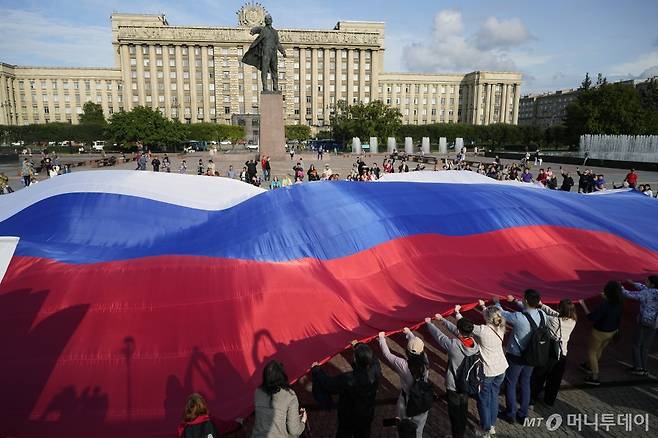 [상트페테르부르크=AP/뉴시스] '러시아 국기의 날'인 22일(현지시각) 러시아 상트페테르부르크에서 시민들이 블라디미르 레닌 동상 앞에 모여 대형 삼색기를 펼치고 있다. 러시아 삼색기는 소련이 붕괴한 1991년 러시아의 공식 국기가 되었고 1994년 러시아 국기의 날이 제정됐다. 2023.08.23. /사진=민경찬