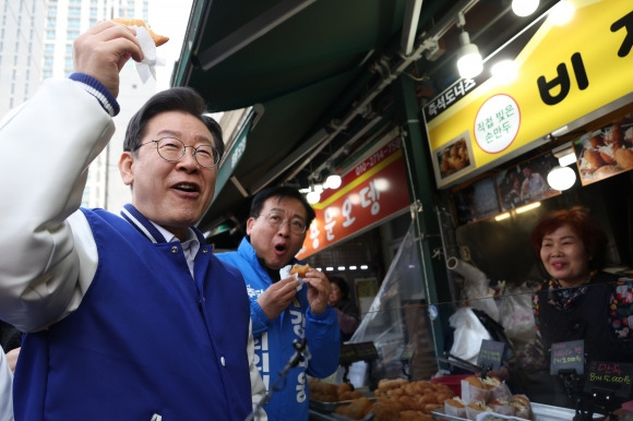 더불어민주당 이재명 대표가 13일 강태웅 후보와 함께 용산구 용문시장을 방문, 상인이 건넨 도넛을 먹고 있다. 2024.3.13 연합뉴스