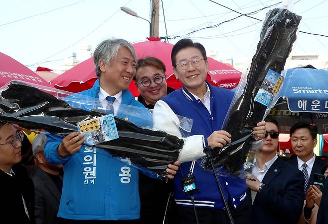 이재명 더불어민주당 대표(오른쪽)가 15일 오후 부산 기장군 기장시장을 방문해 기장군에 출마한 최택용 후보(왼쪽)와 함께 기장군의 특산물인 말린 미역을 들어 보이고 있다.  연합뉴스