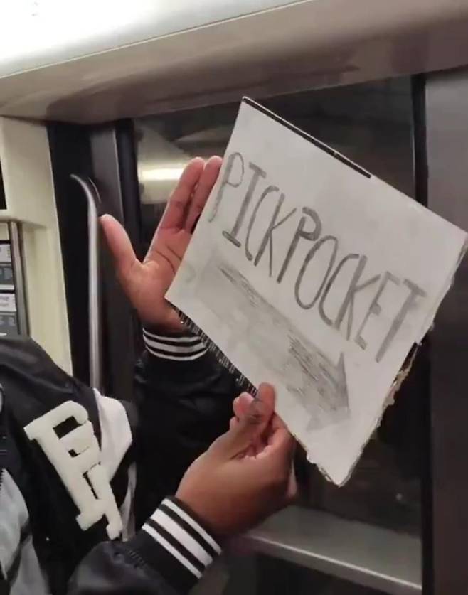 파리 소매치기 고발 영상 속 한 청소년이 영어로 ‘소매치기’라고 적힌 팻말을 들고 있다. X 캡처