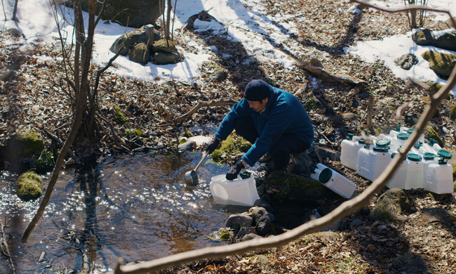 마을의 ‘심부름센터’를 자처하는 타쿠미(오미카 히토시)가 샘에서 물을 뜨고 있다. 그린나래미디어 제공