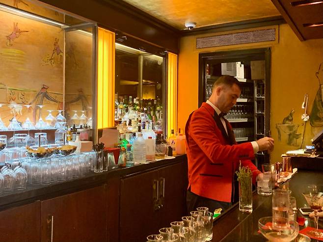 뉴욕 ‘카라일’ 호텔 내부의 ‘베멀먼즈 바(Bemelmans Bar)’. 아르데코 스타일의 인테리어, 금박의 천장아래 새빨간 페라리 색 재킷을 입은 바텐더가 능숙하게 칵테일을 만든다.