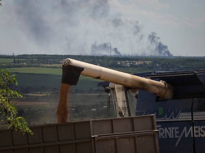 우크라이나 동부 돈바스 지역에서 러시아군의 공격으로 화력 발전소에서 연기가 치솟는 와중에도 곡물 수확 작업이 벌어지고 있다. 스위틀로다르스크/로이터 연합뉴스