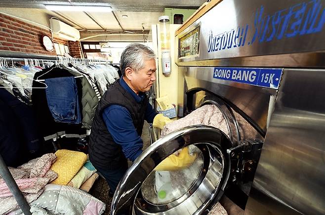 강 사장이 홍 할머니 댁에서 가져온 겨울이불을 세탁소에서 가장 큰 15㎏ 용량 세탁기에 넣고 있다.