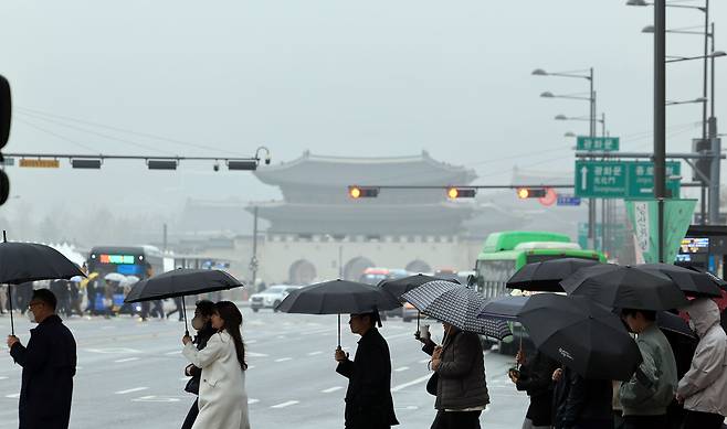 올 봄 최악의 미세먼지 농도를 보이며 ‘황사비’가 내린 29일 오후 서울 종로구 종로구 광화문 네거리에서 우산을 쓴 시민들이 발걸음을 옮기고 있다. /뉴스1