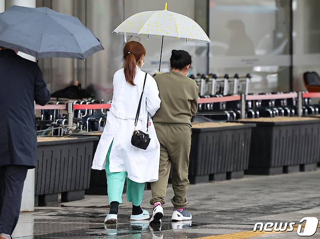 의사 집단행동이 이어지고 있는 29일 서울 시내 한 대학병원에서 의료진과 환자가 우산을 함께 쓰고 길을 지나고 있다. 2024.3.29/뉴스1 ⓒ News1 김도우 기자
