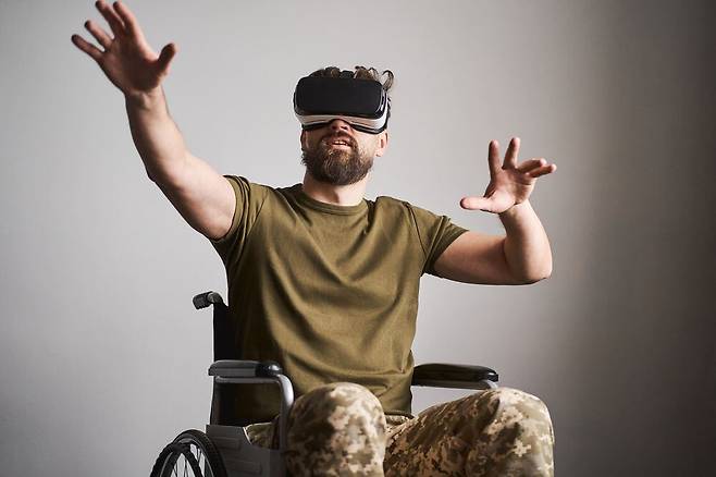 휠체어에 앉아 가상 물체를 만지기 위해 VR 헤드셋을 착용한 상의군인. VR의 의학적 치료는 외상 및 재활에서부터 최근에는 신경질환에 이르기까지 광범위하게 활용되고 있다. /셔터스톡