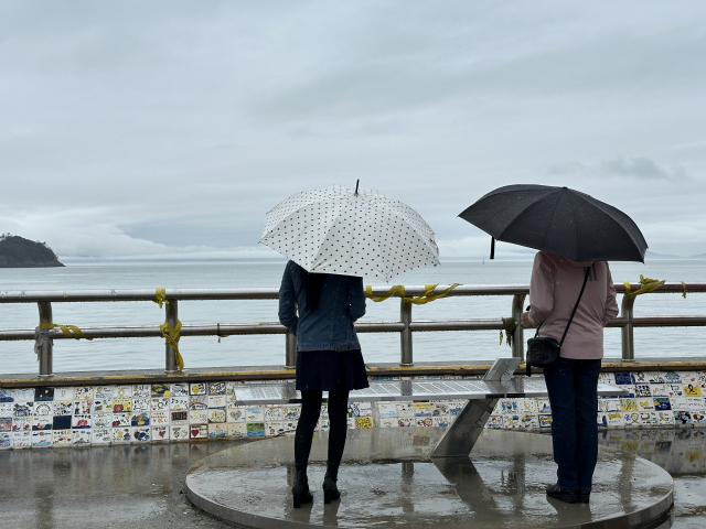 Visitor Chun Sang-mi (left) looks at a bench inscribed with the names of the victims who died in the Sewol ferry disaster, on a seawall near Jindo Port in Jindo, South Jeolla Province. (Lee Jung-joo/The Korea Herald)
