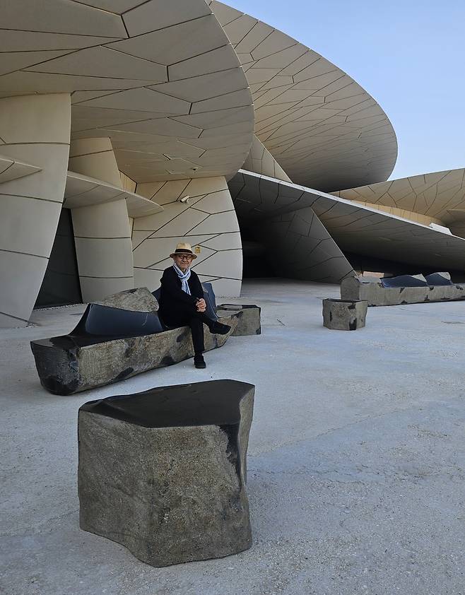 Choi Byung-hoon poses for a photo sitting on his sculpture "Afterimage of the Beginning 2023" on Feb. 25 at the National Museum of Qatar in Doha, Qatar. (Park Yuna/The Korea Herald)