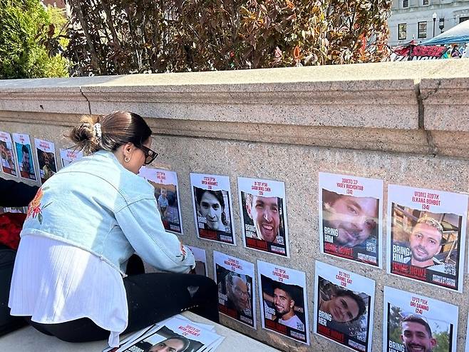 한 컬럼비아대 학생이 천막 농성장 근처에 하마스한테 납치당한 이스라엘인들 사진을 붙이고 있다.