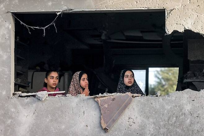 24일(현지시각) 팔레스타인 가자지구 남부 도시 라파흐에서 소녀들이 폭격으로 부서진 창문 너머로 밖을 내다보고 있다. 라파흐/AFP 연합뉴스