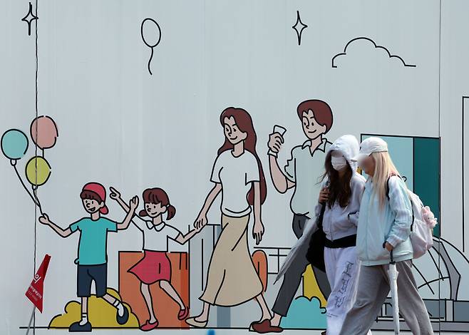 서울 도심의 공사장 가림막에 그려진 행복한 가족 그림 앞으로 시민이 지나고 있다./뉴스1