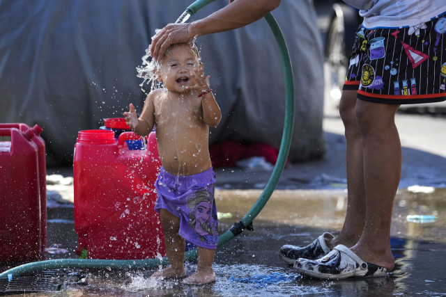필리핀 마닐라에서 한 남성이 무더위를 식히기 위해 아이에게 물을 뿌려주고 있다. /AP연햡뉴스
