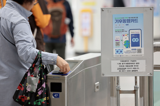 A person passes through a subway turnstile at Gwanghwamun Station in central Seoul on April 7 with a banner advertising the Climate Card unlimited public transportation pass displayed nearby. [YONHAP]