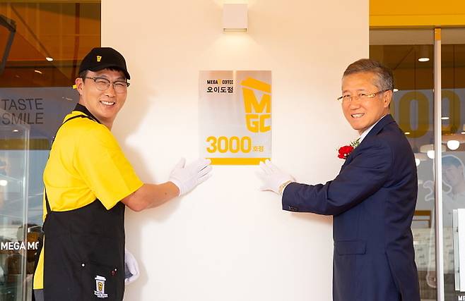 지난 9일 김대영 메가MGC커피 대표이사(오른쪽)와 이종욱 오이도점주가 시흥 오이도점에서 3000호점 오픈 현판식을 갖고 기념 촬영을 하고 있다.