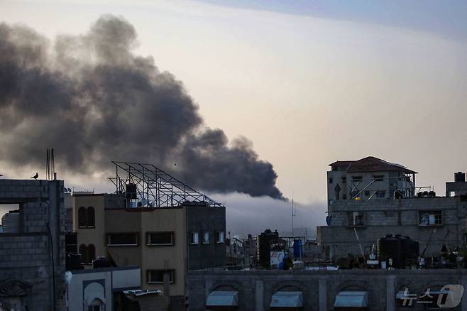 10일 동 트는 남부 가자 라파의 무너진 건물 사이로 이스라엘군 포격에 당한 건물에서 뿜어져 나오는 검은 연기가 하늘을 덮고 있다. 2024.05.10 ⓒ AFP=뉴스1 ⓒ News1 정지윤기자