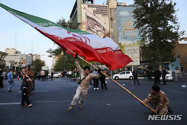 [테헤란=AP/뉴시스] 지난달 19일(현지시각) 이스라엘이 이란에 재보복 공격을 단행했다. 지난 4월15일 사진에서 이란 테헤란에서 반이스라엘 메시지가 그려진 한 건물 앞에서 시위대가 커다란 이란 국기를 흔들고 있다. 2024.05.12.